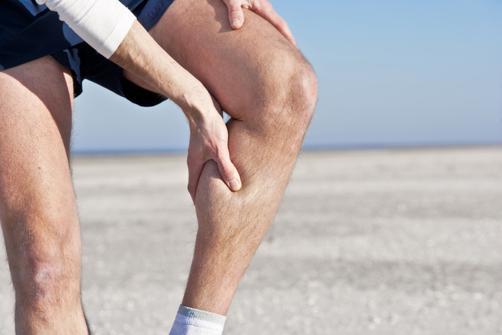 Man suffering from a leg cramp, massaging it with his hand.