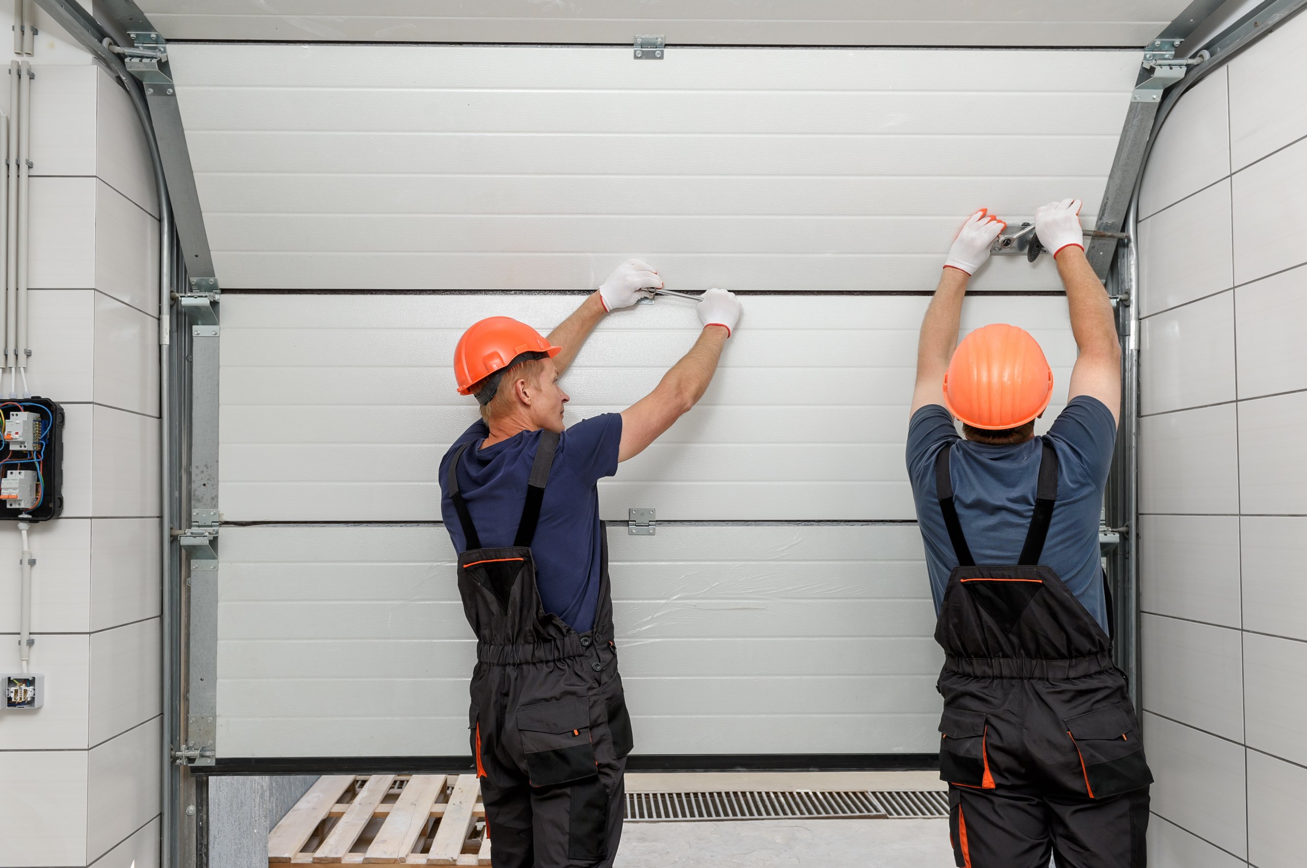 Two men are actively working on a garage door maintenance, focused on their task.Two men are actively working on a garage door maintenance, focused on their task.