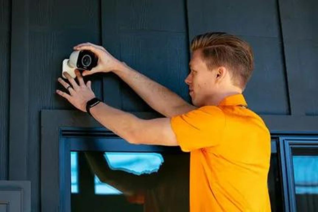 a man in a yellow shirt is installing a home security camera