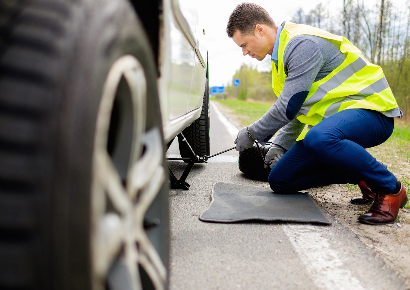 roadside assistance expert working on a car tire on the side of the road